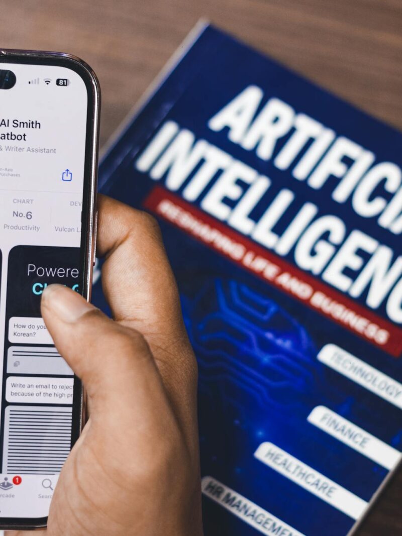 Smartphone displaying AI app with book on AI technology in background.
